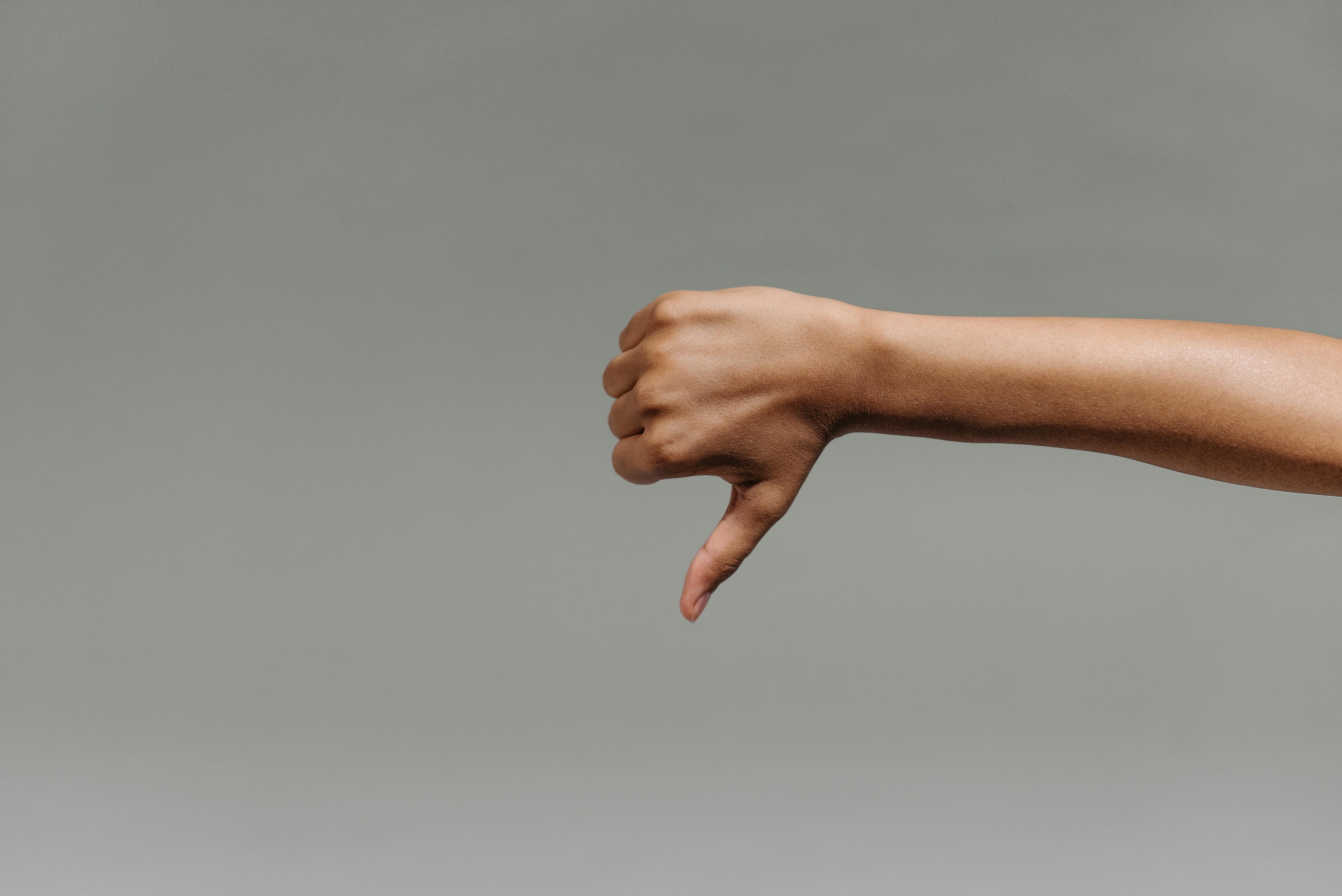 Geste de désapprobation avec un bras et une main sur fond gris, symbolisant un avis négatif ou l’insatisfaction client