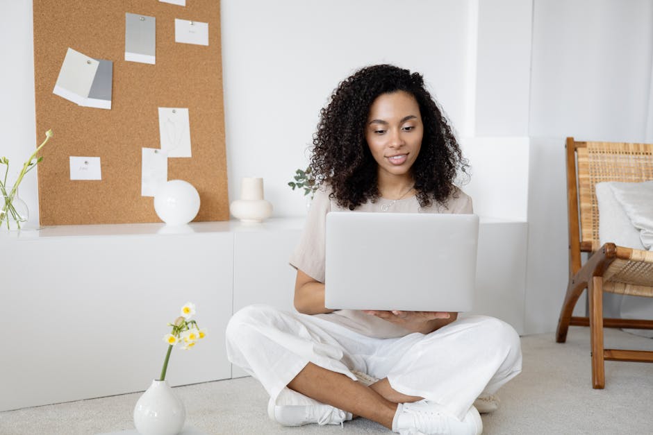 Jeune femme aux cheveux bouclés travaillant sur ordinateur dans un cadre domestique chaleureux, dégageant assurance et concentration