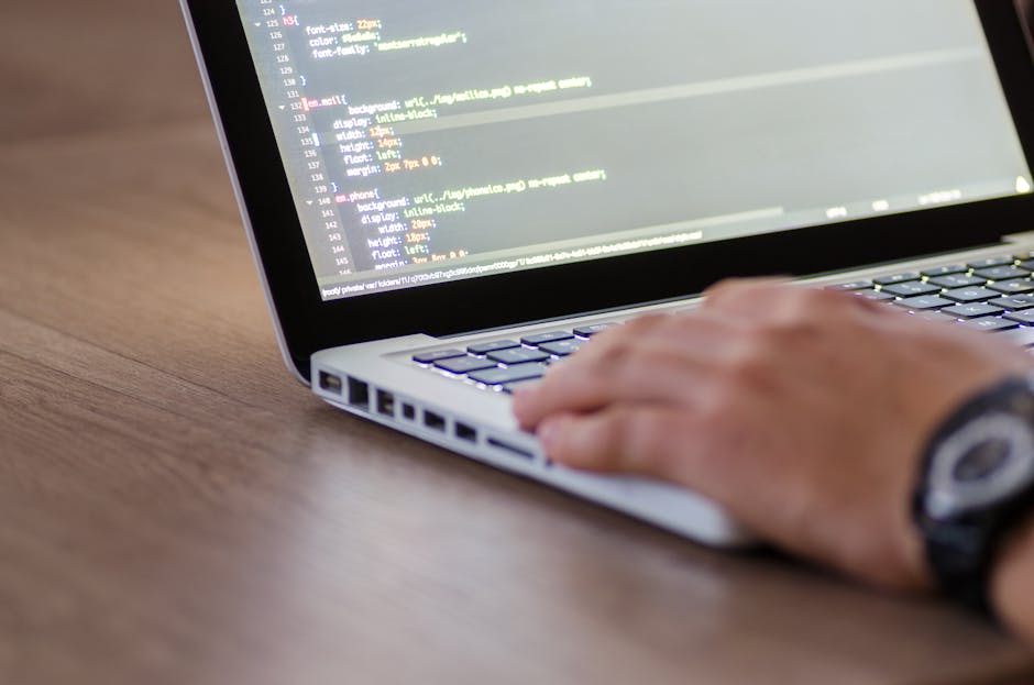Personne codant sur un ordinateur portable avec du code HTML à l'écran, illustrant un travail de développement.