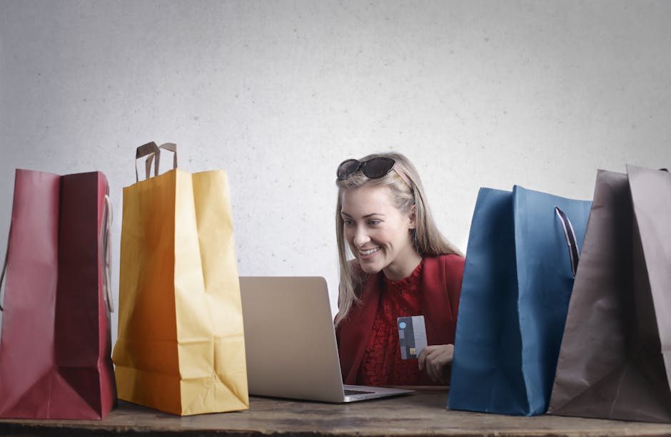 Une femme satisfaite effectue des achats en ligne sur son ordinateur portable, entourée de sacs shopping multicolores.
