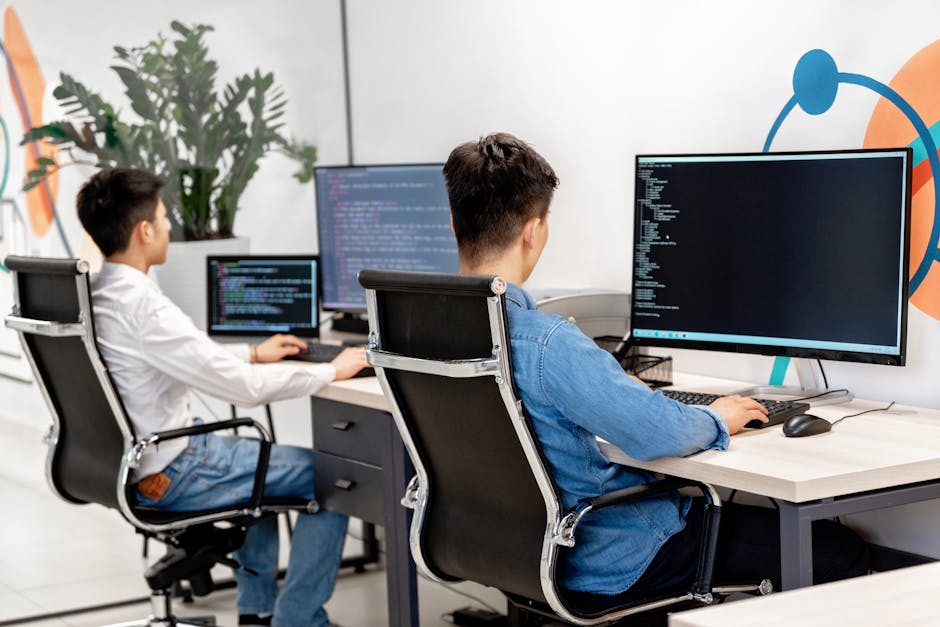 Deux développeurs masculins programmant dans un bureau moderne équipé de grands écrans.