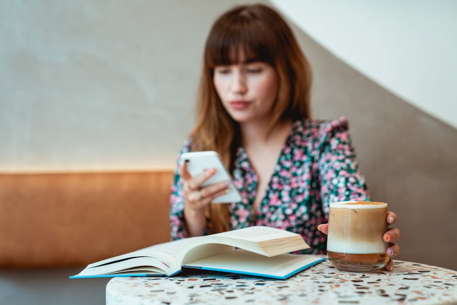 Une femme détendue dans un café avec un latte, un smartphone et un livre, profitant de son temps libre.