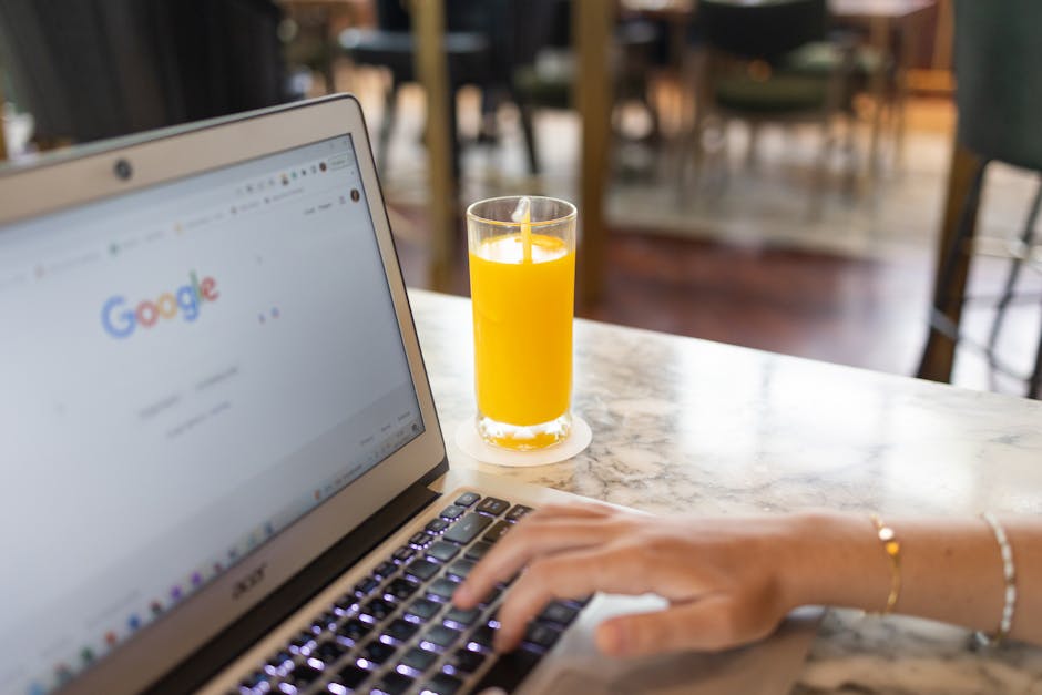 Woman working on laptop with Google homepage open, next to a glass of orange juice on a marble table.