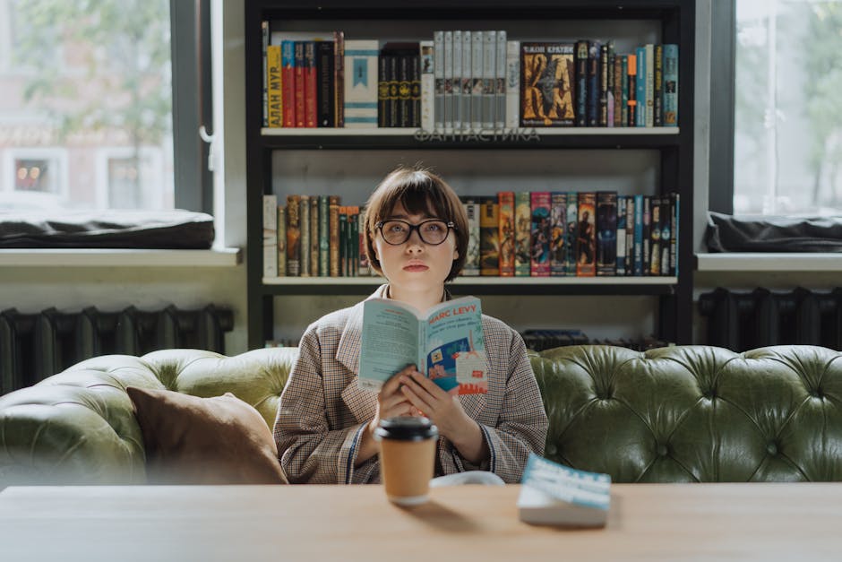 Une jeune femme profite d'un moment de lecture dans une bibliothèque cosy, un livre à la main et un café posé sur la table.