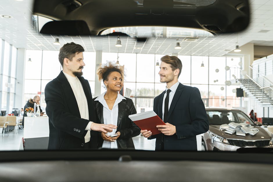 Un groupe de trois personnes discutant des options d'achat de voitures à l'intérieur d'un concessionnaire.