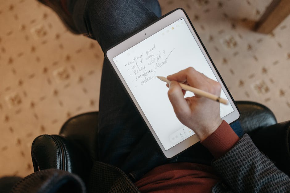 Gros plan d'une personne écrivant sur une tablette avec un stylet dans un environnement intérieur confortable.