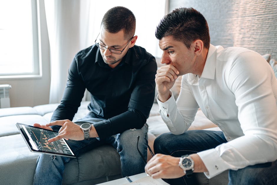 Deux hommes d'affaires analysant des données financières sur une tablette en intérieur.