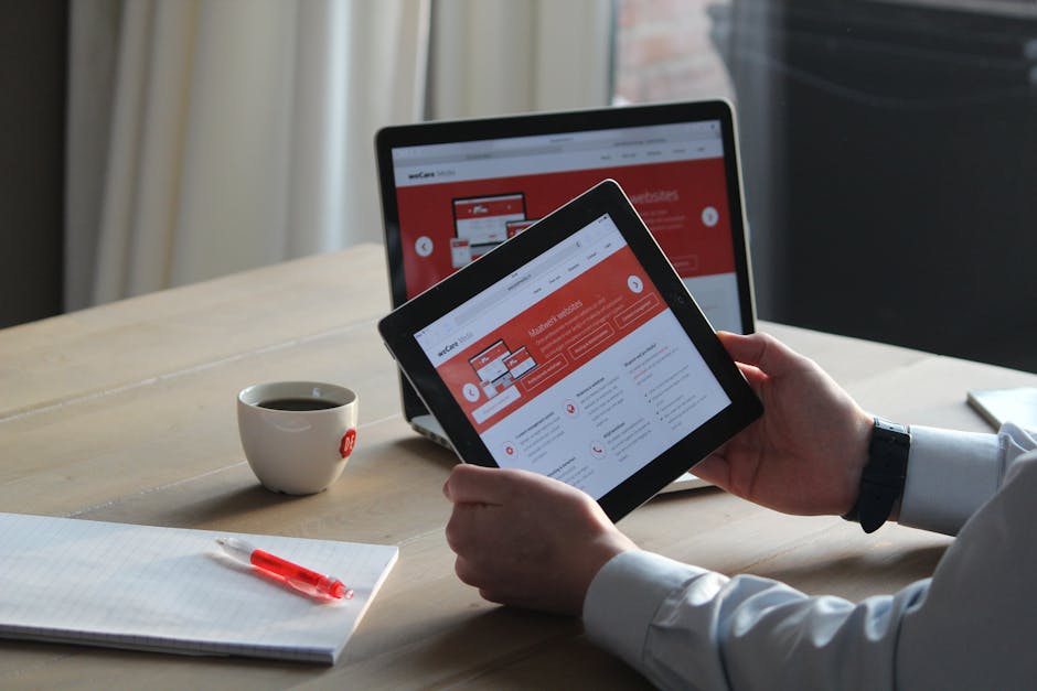 Professionnel utilisant une tablette et un ordinateur portable avec une boisson chaude, concentré sur la consultation de contenu digital.