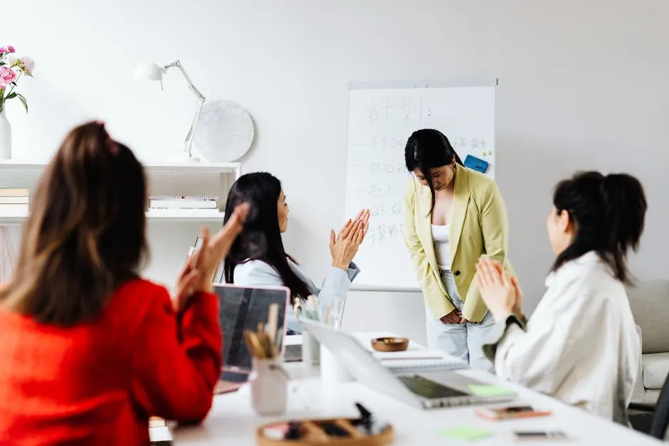 Asian women in an office setting clapping for a colleague after a presentation with a whiteboard in the background.