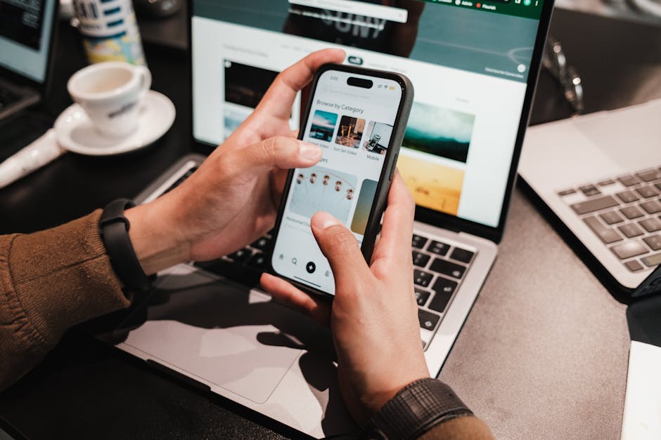 Gros plan sur des mains utilisant un smartphone au-dessus d'un ordinateur portable dans un cadre de bureau moderne.