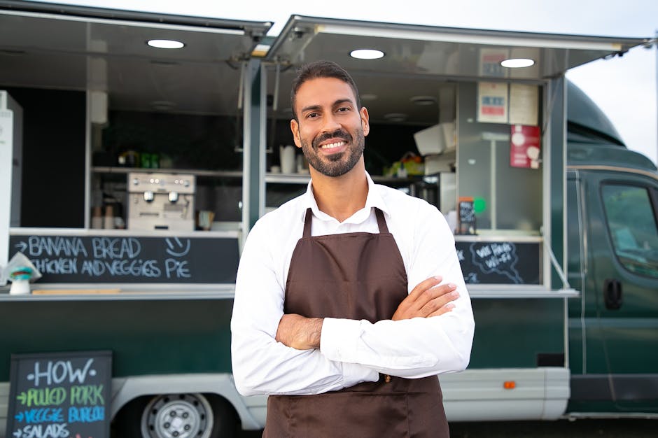 Jeune serveur souriant en tablier croisant les bras devant un food truck moderne