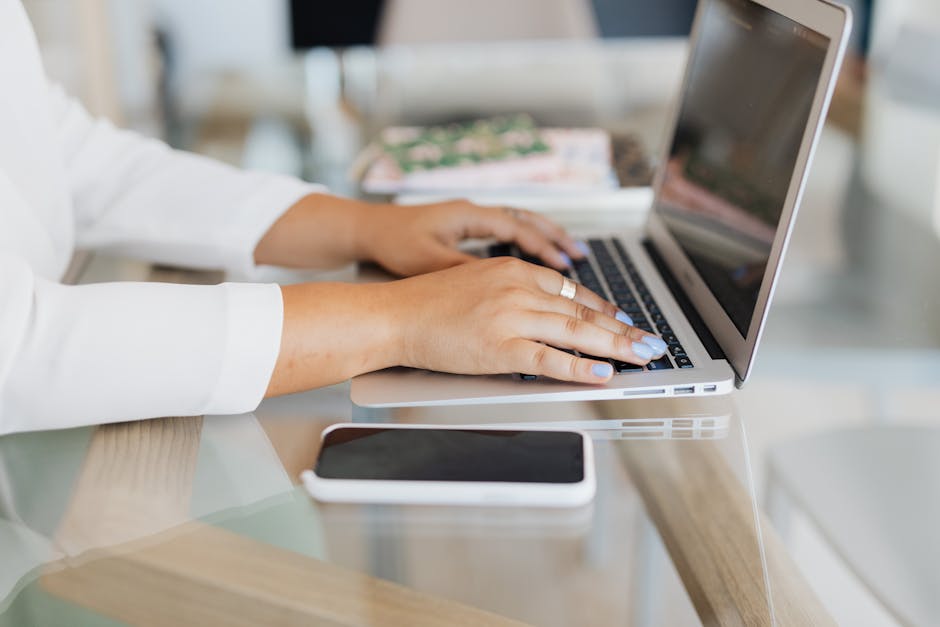 Gros plan de mains tapant sur un ordinateur portable avec un smartphone sur le bureau.