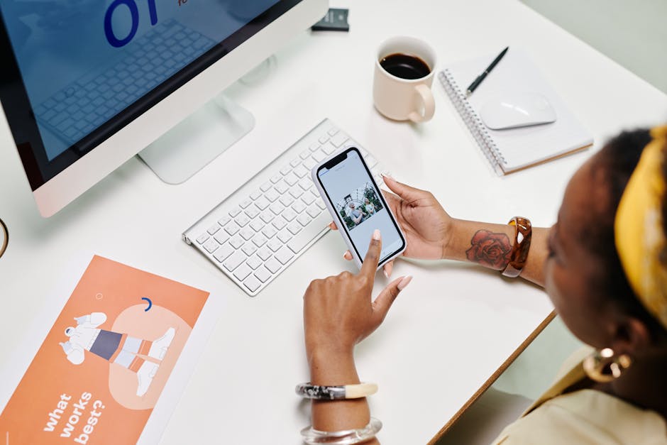 Vue aérienne d'une femme à son bureau utilisant un smartphone et un ordinateur, entourée d'objets de bureau.