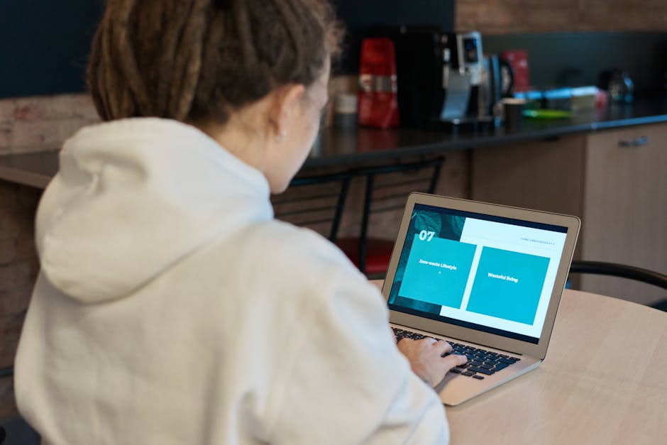 Una mujer con una sudadera blanca trabaja en su computadora portátil, concentrada en un acogedor café.