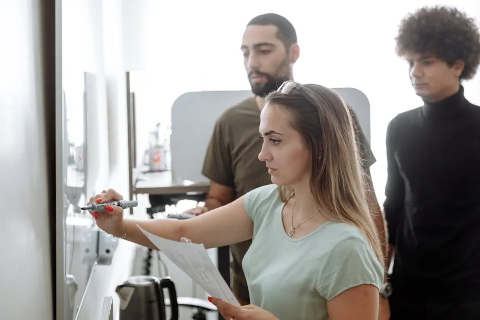 Three young professionals brainstorming around a whiteboard in a modern office.