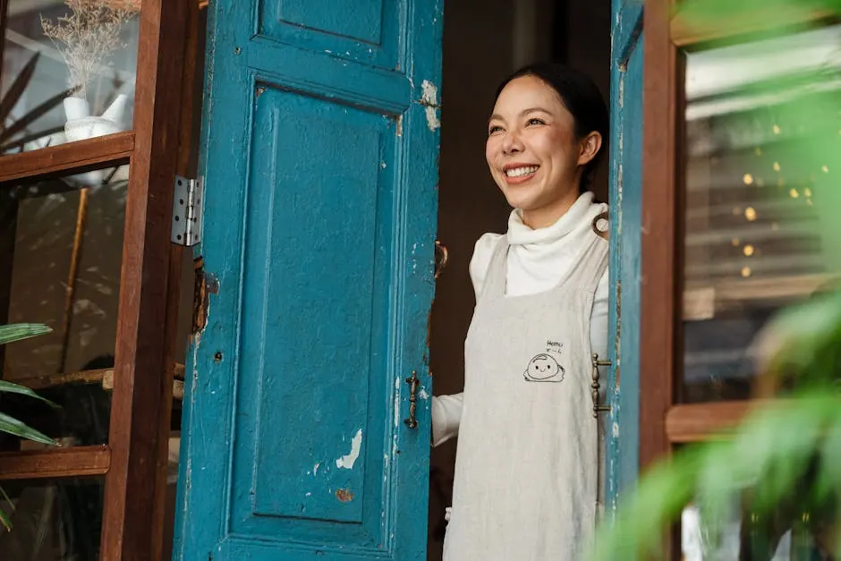 Smiling young woman in an apron welcoming customers at the entrance of a cozy café