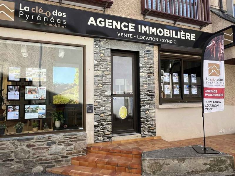 Escaparate de la agencia inmobiliaria La Clé des Pyrénées, fachada de piedra y anuncios en el escaparate